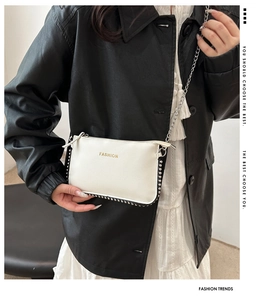 Close-up of white pebble leather envelope bag with silver studs and FASHION lettering