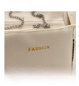 Detail of cream lychee texture leather bag with gold FASHION logo and silver chain strap