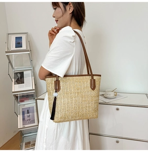 Detail of large woven straw tote bag with brown leather trim and tassel on a model