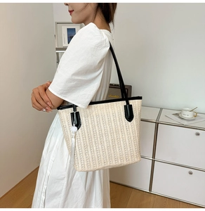 Detail of large woven straw tote bag with black PU leather straps and white tassel charm