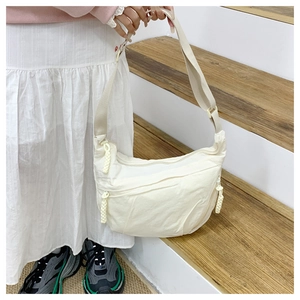 Detail of white crescent crossbody bag showing textured nylon fabric and rope zipper pull