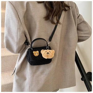 Detail einer schwarzen Teddy-Umhängetasche mit Plüschbär-Anhänger an einem Model
