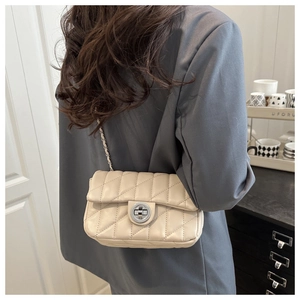 Détail du sac beige matelassé à chaîne argentée porté par un mannequin en intérieur