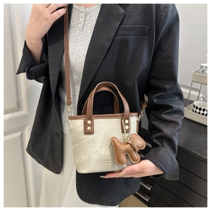 Detail der minimalistischen Bucket Bag aus Segeltuch mit braunen Ledergriffen und Anhänger