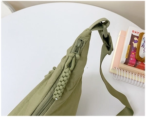 Detail of green nylon crossbody bag featuring woven zipper pull and adjustable strap
