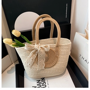 Details der handgewebten Strohtasche mit braunem Kreismuster und Spitzen-Schleife