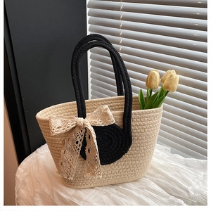 Detail der handgewebten Strohtasche mit eleganter Spitzenschleife und schwarzen Seilgriffen