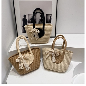 Drei Varianten von gewebten Stroh-Tote-Bags mit Spitzenanhängern auf minimalistischem Display