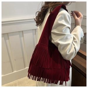 Detail shot of long layered tassels on a burgundy suede tote bag styled with a blazer