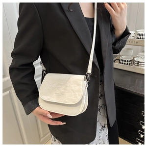 Détail d'un sac bandoulière crème minimaliste avec plis texturés et typographie mode