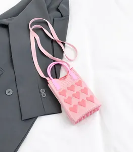Detail of pink knitted crossbody bag featuring 3D textured heart patterns and wide strap