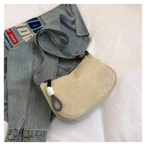 Detail der beigen Cord-Umhängetasche mit gestreiftem Gurt auf einer Denim-Jacke