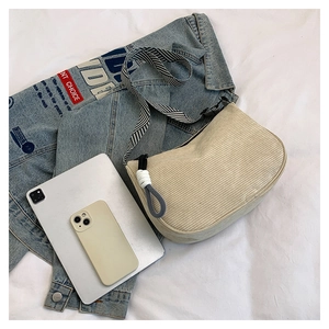 Detail der Cord-Halbmondtasche mit gestreiftem Canvas-Gurt und Seilquasten-Accessoire