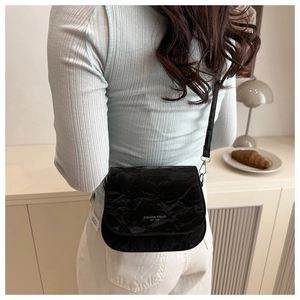 Détails d'un sac à bandoulière noir minimaliste avec texture plissée et logo blanc