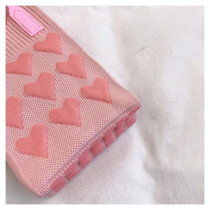 Primer plano de bolso de punto rosa con corazones en relieve y detalle de correa de cuero