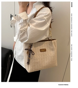Detail of hand-woven straw tote bag featuring brown leather strap and chic ribbon bow