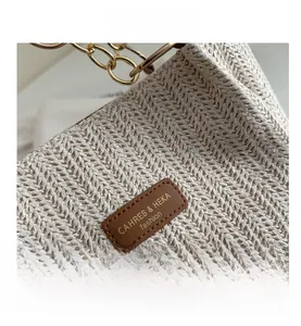 Detail of herringbone woven straw tote bag with gold chain handle and leather logo tag