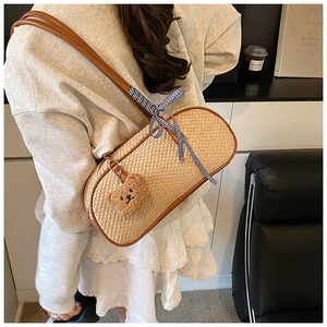 Detail van beige gevlochten schelptas met leren riem en decoratieve beer hanger