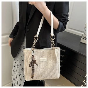Detail of straw woven tote bag featuring white leather straps and golden chain accents