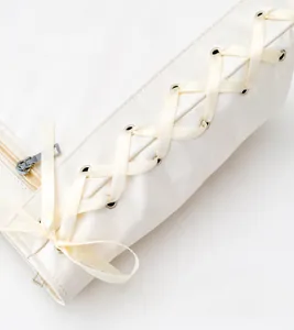 Detail of cream tote with silk ribbon lacing through silver eyelets on side panel