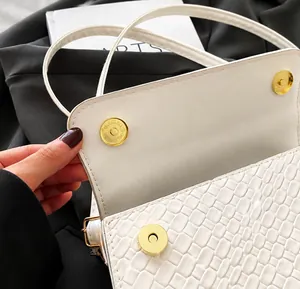 Close-up of magnetic snap closure on white embossed faux leather crossbody bag