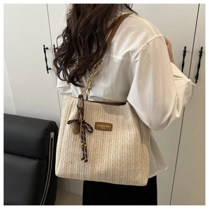 Close-up of woven straw tote bag with brown leather logo and metallic chain strap