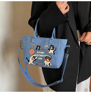 Detail of light blue denim tote bag with cute cartoon cat prints and sturdy top handles
