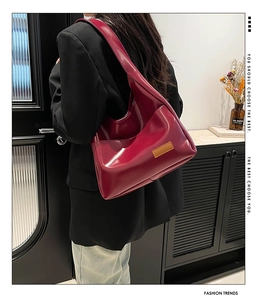 Detail of dark red tote bag in glossy faux leather worn by model in a modern room