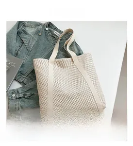 Détail du sac fourre-tout tissé en paille beige sur table avec veste en jean et magazine