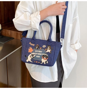 Detail of blue denim tote bag featuring cartoon embroidery and adjustable shoulder strap