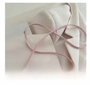 Detailed close-up of pink crossbody bag with refined stitching on beige suit fabric
