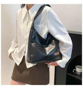 Detail of minimalist black PU leather hobo bag with a brown tag and wide strap
