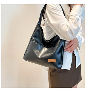 Detail of a black leather shoulder bag with a brown logo patch worn with casual outfit