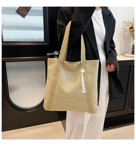 Détail d'un sac cabas en paille tressée avec gland blanc et larges anses en tissu