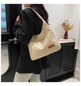 Detail of a large cream-colored faux leather tote bag showing glossy texture and shoulder strap