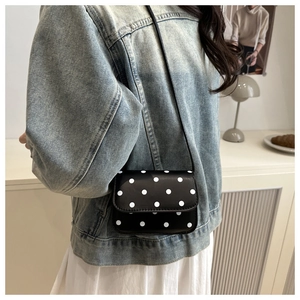 Detail of a black polka dot mini crossbody bag with a slim strap worn over a denim jacket