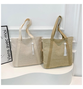 Détail de la texture d'un sac cabas en paille tissée avec anses et pompons blancs décoratifs