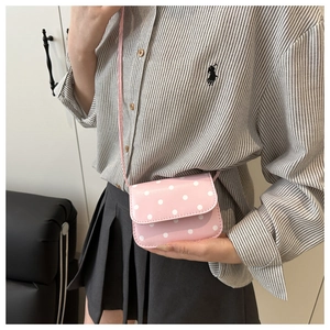 Detailed view of pink polka dot crossbody bag with flap closure and matching shoulder strap