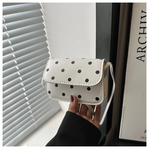 Close-up of a white crossbody bag with black polka dots and fine PU leather texture