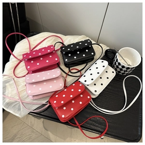 Close-up of small crossbody polka dot flap bags in five vibrant colors on a wooden table