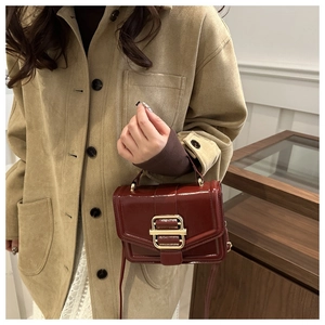 Detailed shot of a burgundy glossy leather handbag with a large square gold metal buckle