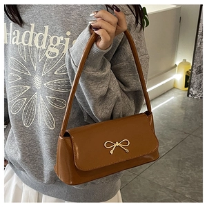 Détail d'un sac baguette en cuir verni marron avec une boucle dorée en forme de nœud