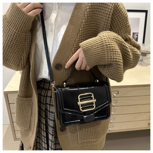 Detail of a black patent leather crossbody bag with a distinctive gold square buckle