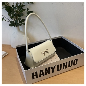 Détail d'un sac baguette blanc crème avec boucle en nœud doré dans un coffret cadeau