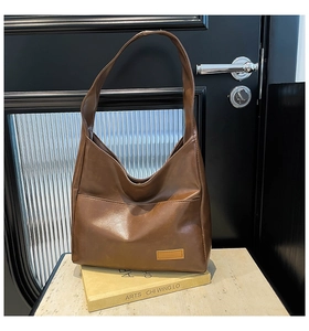 Detail view of a brown leather tote bag with rectangular patch on a minimalist background