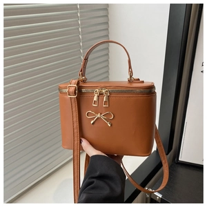 Detail of a brown leather box bag featuring a gold bow accent and zip-around closure