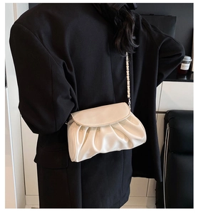 Detail of white pleated cloud bag with silver woven chain strap on a black blazer