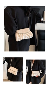 Detail of creamy white pleated cloud bag with golden chain strap on black blazer