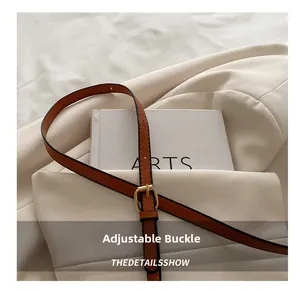Detail of golden metal adjustment buckle on the brown leather strap of a vintage bag