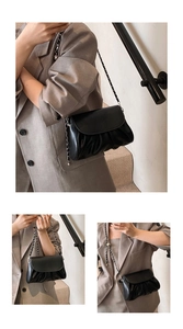 Close-up of black pleated cloud bag with silver metal chain strap and spherical charm detail